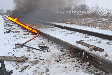 CN's Dubuque Subdivision came apart during an overnight run in frigid temperatures on January 10, 2016; section crews spent forty-eight hours chasing down broken rails. At MP 269.9, just west of Raymond, Iowa, the crew gets to work by burning a fiberglass rope against the rail to expand it. Their tools are in place to realign the rail. 

Judges' comments: A broken rail in winter visually narrates the constant battle with nature that the men and women who maintain railroads must endure. The photographer deftly presents the track crew as they heat and align adjacent sections of rail. Hydraulic jacks, sledge hammers, sweat, snow, and flames all shape this memorable series.

Read more about the 2021 John E. Gruber Creative Awards Program: <a href="https://railphoto-art.org/awards/2021-awards/" rel="noreferrer nofollow">railphoto-art.org/awards/2021-awards/</a>