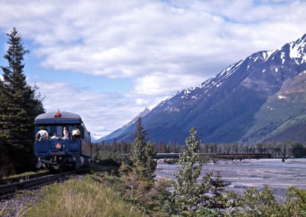 People enjoying the view from the <i>Glacier Express</i> business car aboard a southbound Alaska Railroad special passenger train crossing the Snow River near Seward, Alaska, in c. 1968. Photograph by Leo King, © 2015, Center for Railroad Photography and Art. King-02-005-012