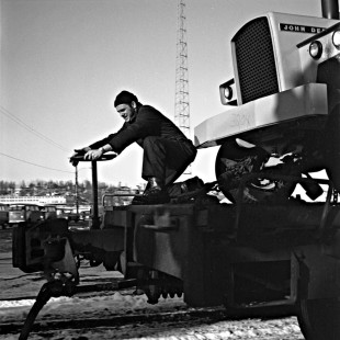 Alaska Railroad trainman tying down a handbrake on a flatcar carrying John Deere equipment in Anchorage, c. 1970. Photograph by Leo King, © 2015, Center for Railroad Photography and Art. King-03-002-008