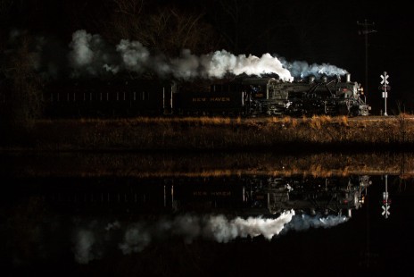 The Valley Railroad's Essex Steam Train is reflected by the Connecticut River at Pratt Cove in Deep River, Connecticut, on December 18, 2012. The photographer, drawing inspiration from O. Winston Link, Richard Steinheimer, and Mel Patrick, lit the scene with three electronic flashes. He used Adobe Lightroom to remove one small streetlight from the among the tree branches at upper left and its reflection in the water.
