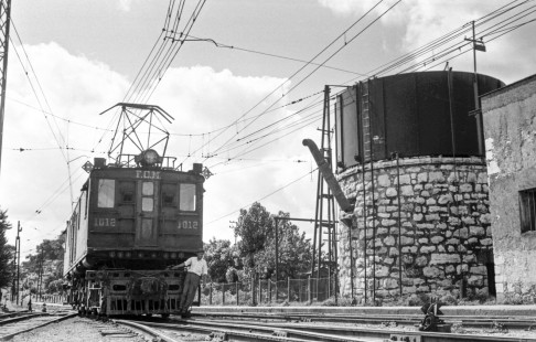 Worker rides the front of Mexican Railway electric boxcab no. 1012 next to water tower at Orizaba, Veracruz, Mexico on August 28, 1961. Rose-01-183-33; Photograph by Ted Rose,  © 2015, Center for Railroad Photography and Art