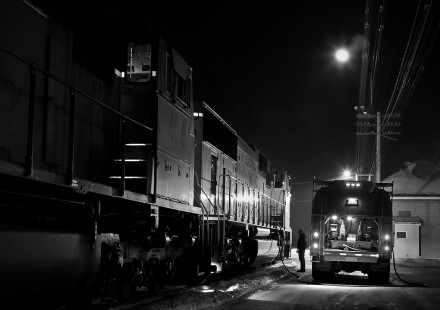 <strong>Travis Dewitz, Altoona, Wisconsin</strong>
February 22, 2008. The moon gently lights the urgent operation of a delivery driver fueling a locomotive. The train somehow made it out of the main terminal in St. Paul, Minnesota, without enough diesel fuel for its journey.

<strong>Judge's Comment:</strong>
Night work. Love it!