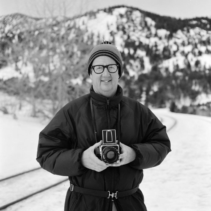 Ron Hill holding camera in a portrait by Jeff Brouws
